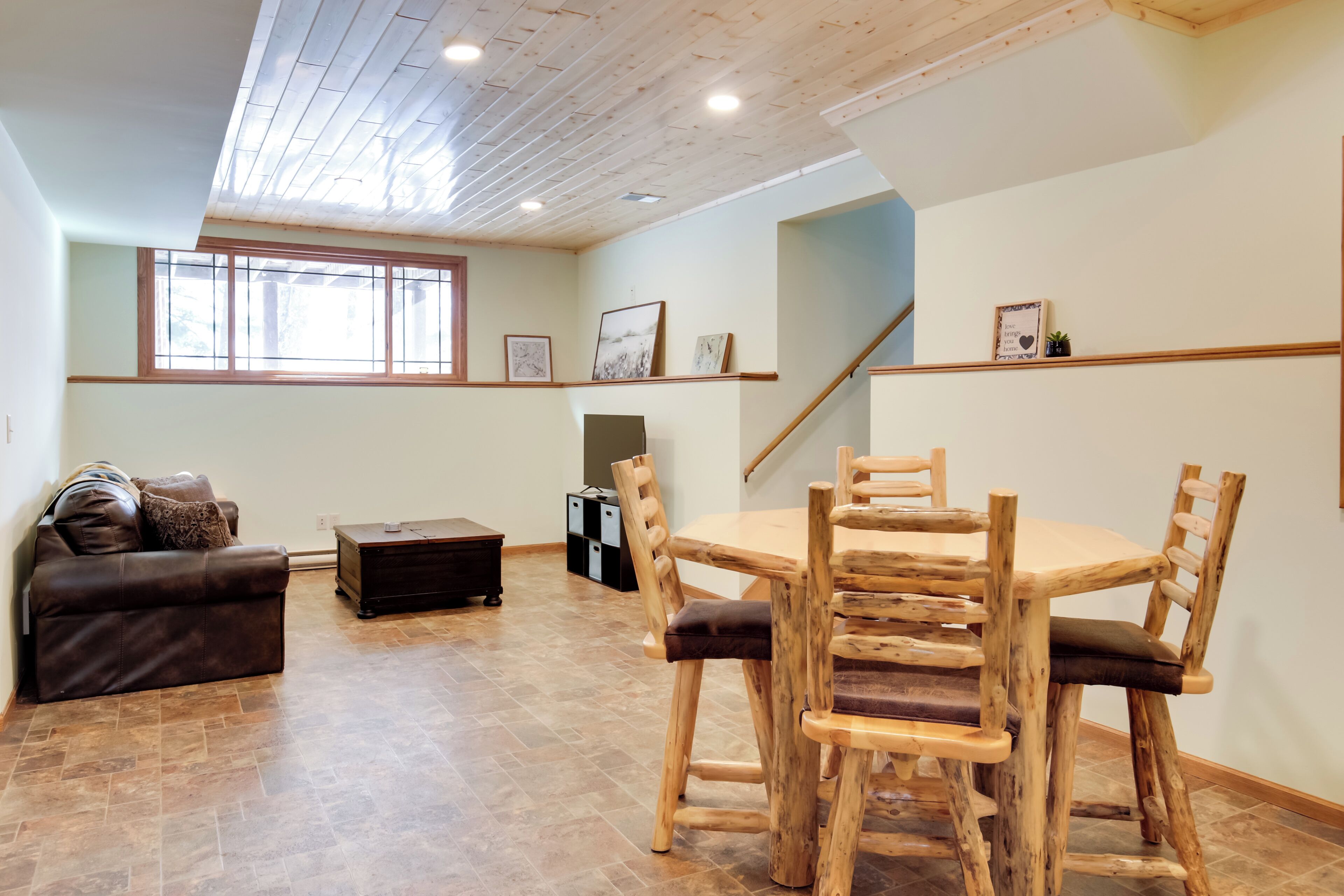 A spacious living room with a wooden dining table and chairs, a leather sofa, and a staircase leading to another level.