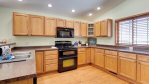 Une cuisine avec des meubles de rangement en bois, un four à micro-ondes, une cuisinière et une fenêtre avec des stores.