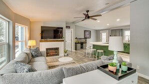 Una sala de estar moderna con chimenea, sofá gris y comedor con taburetes de bar.