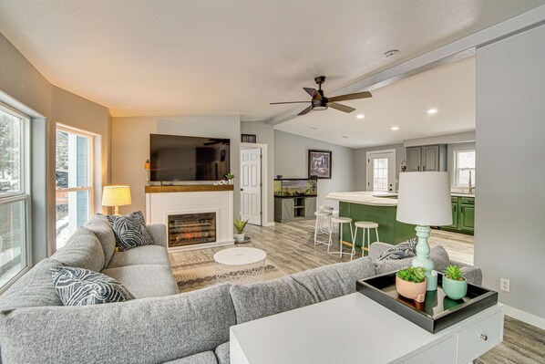 A modern living room with a fireplace, grey sofa, and a dining area with bar stools.