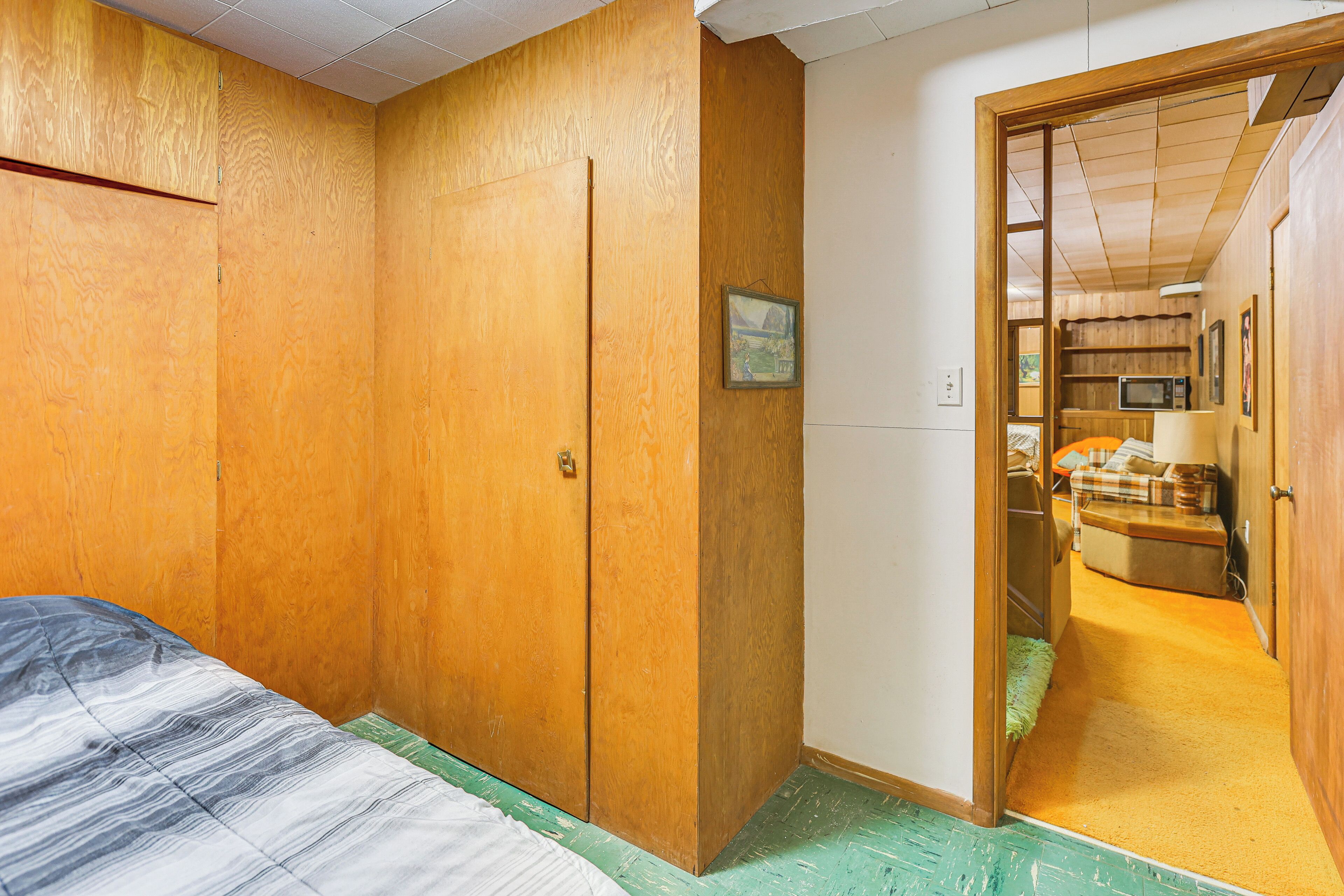 A bedroom with a bed, wooden wardrobe, and a door leading to a kitchen area.