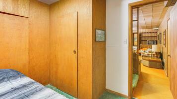 A bedroom with a bed, wooden wardrobe, and a door leading to a kitchen area.