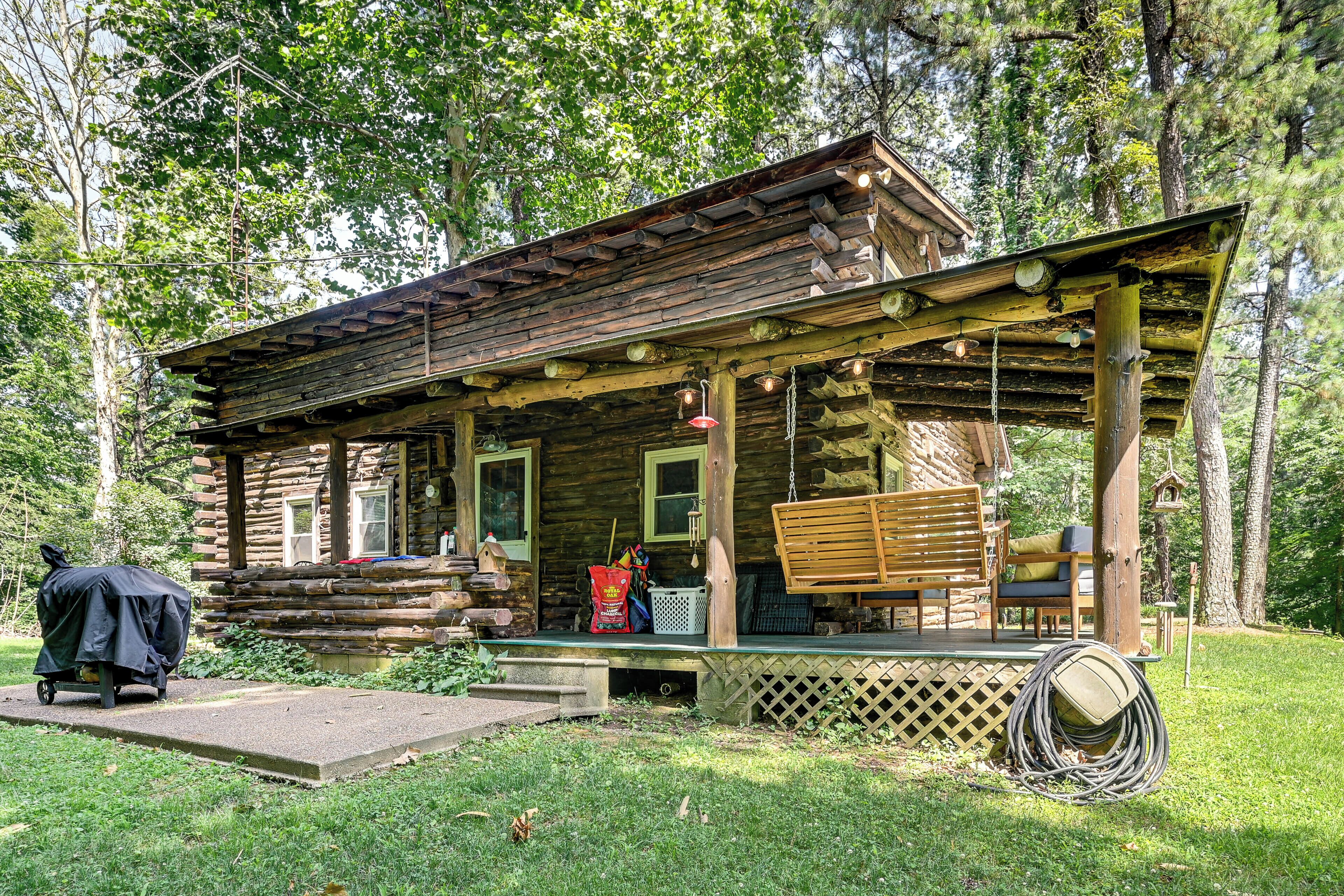 A rustic log cabin with a porch, outdoor seating, and a covered grill area.