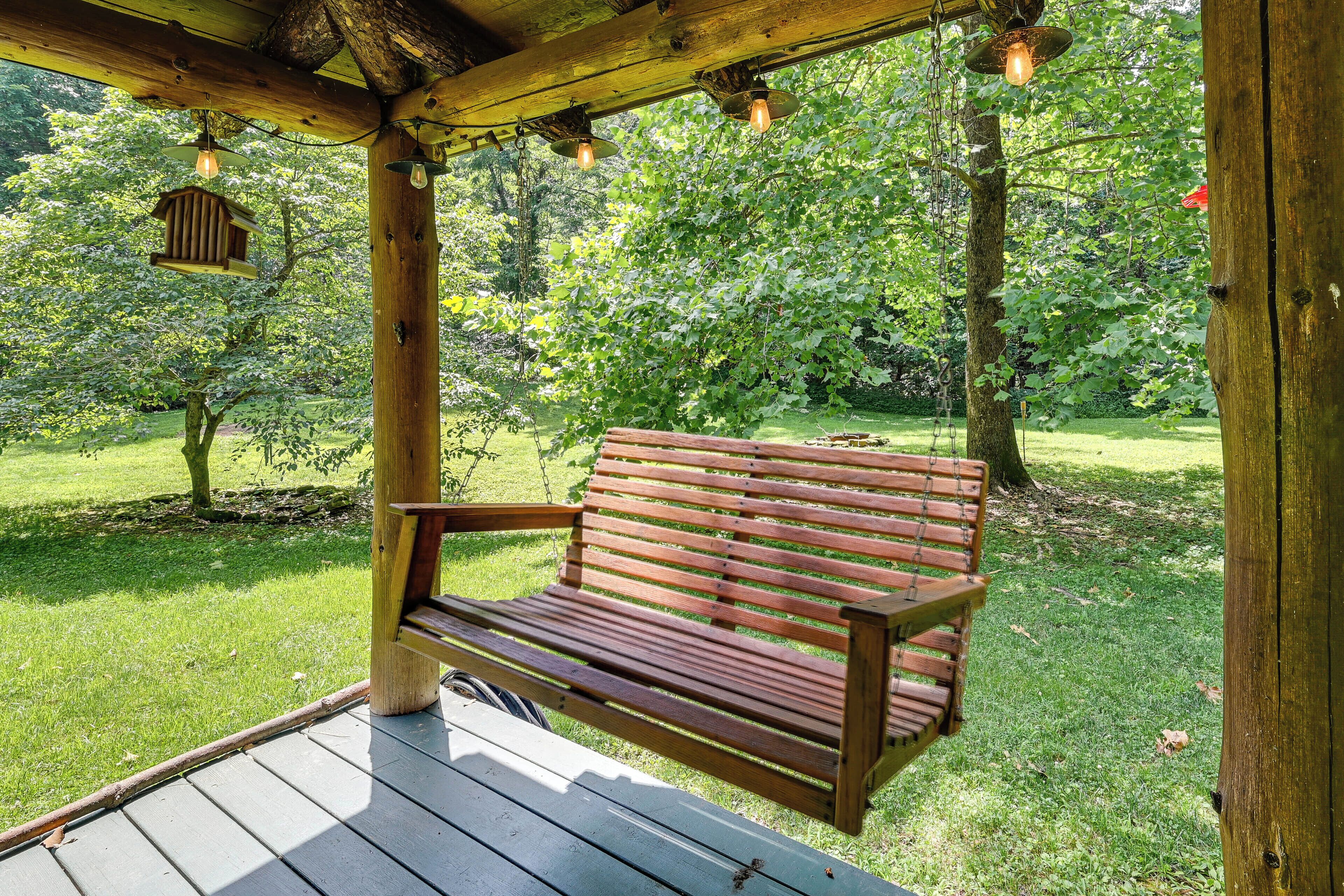 Un banco de madera bajo una pérgola de madera con luces colgantes, rodeado de un exuberante jardín verde.