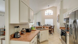 A kitchen with white cabinets, a built-in oven, a refrigerator, and a coffee maker. - 9 Mi to Disney: Home w/ Pool Table & Water Views! (Kissimmee)