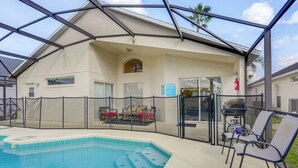 A covered outdoor swimming pool area with a glass enclosure, lounge chairs, and a barbecue grill. - 9 Mi to Disney: Home w/ Pool Table & Water Views! (Kissimmee)