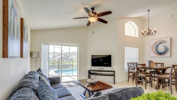 A living room with a sofa, TV, ceiling fan, dining table, and chairs. - 9 Mi to Disney: Home w/ Pool Table & Water Views! (Kissimmee)