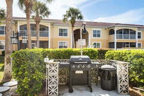 A barbecue grill and trash can in front of a building with balconies and palm trees. - 8 Mi to Beach: Modern Condo in Fort Myers! (Fort Myers)