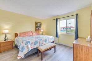 A bedroom with a bed, bedside tables, a bench, a window with curtains, and a painting on the wall.