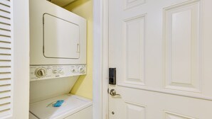 Un cuarto de lavado con lavadora y secadora de carga frontal, una puerta con cerradura electrónica y una ventana con persianas.