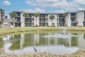 A multi-story residential building with balconies, a pond with a fountain, and palm trees.