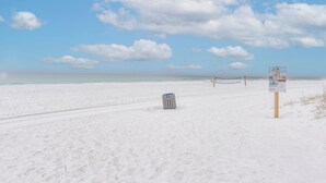 Una playa con un cartel, un basurero y un cielo despejado.