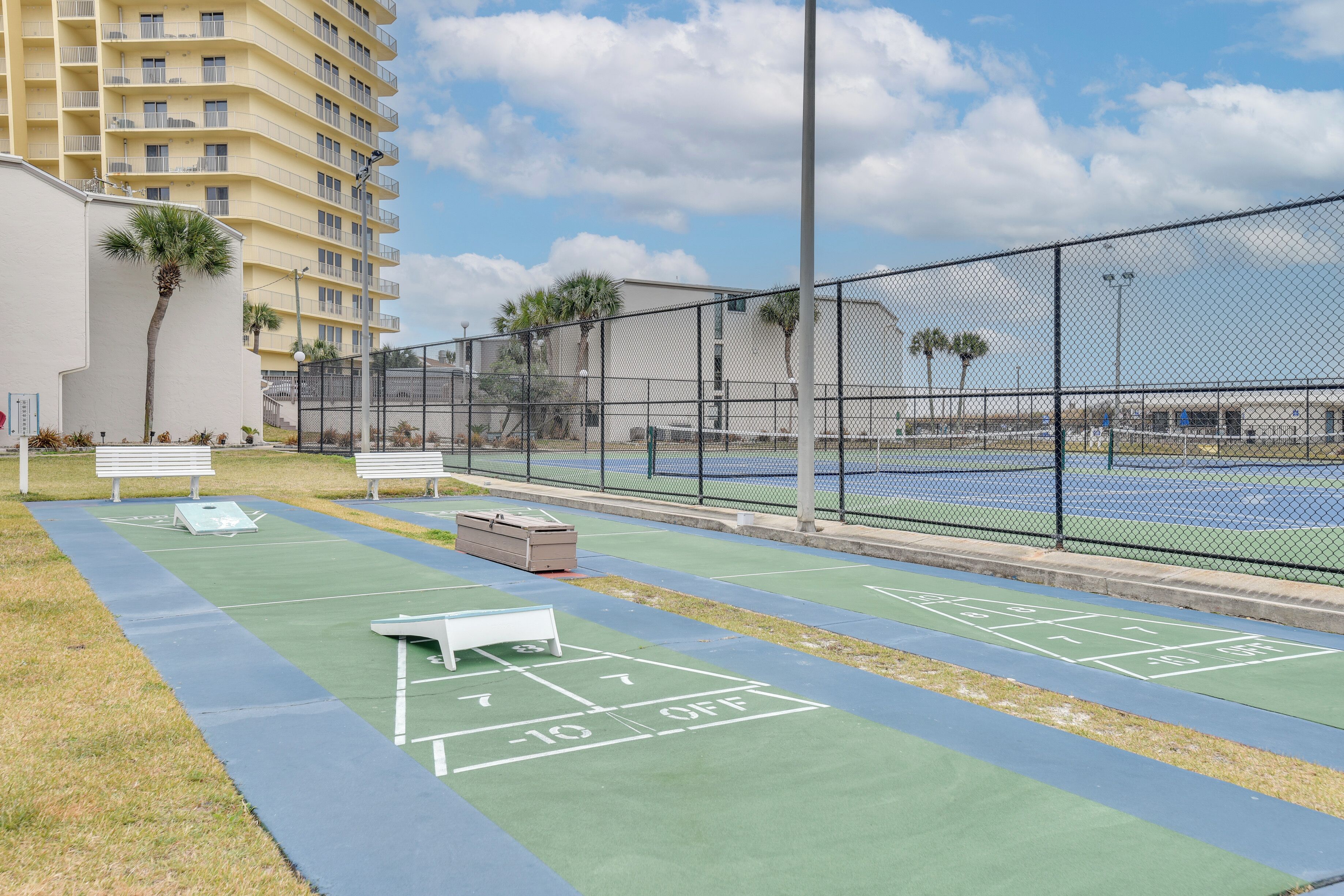 Una cancha de tenis con superficie verde y líneas delimitadoras blancas, rodeada por una cerca de malla metálica.