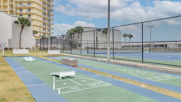 Una cancha de tenis con superficie verde y líneas delimitadoras blancas, rodeada por una cerca de malla metálica.