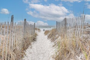 A sandy path flanked by wooden fences leading to a beach.