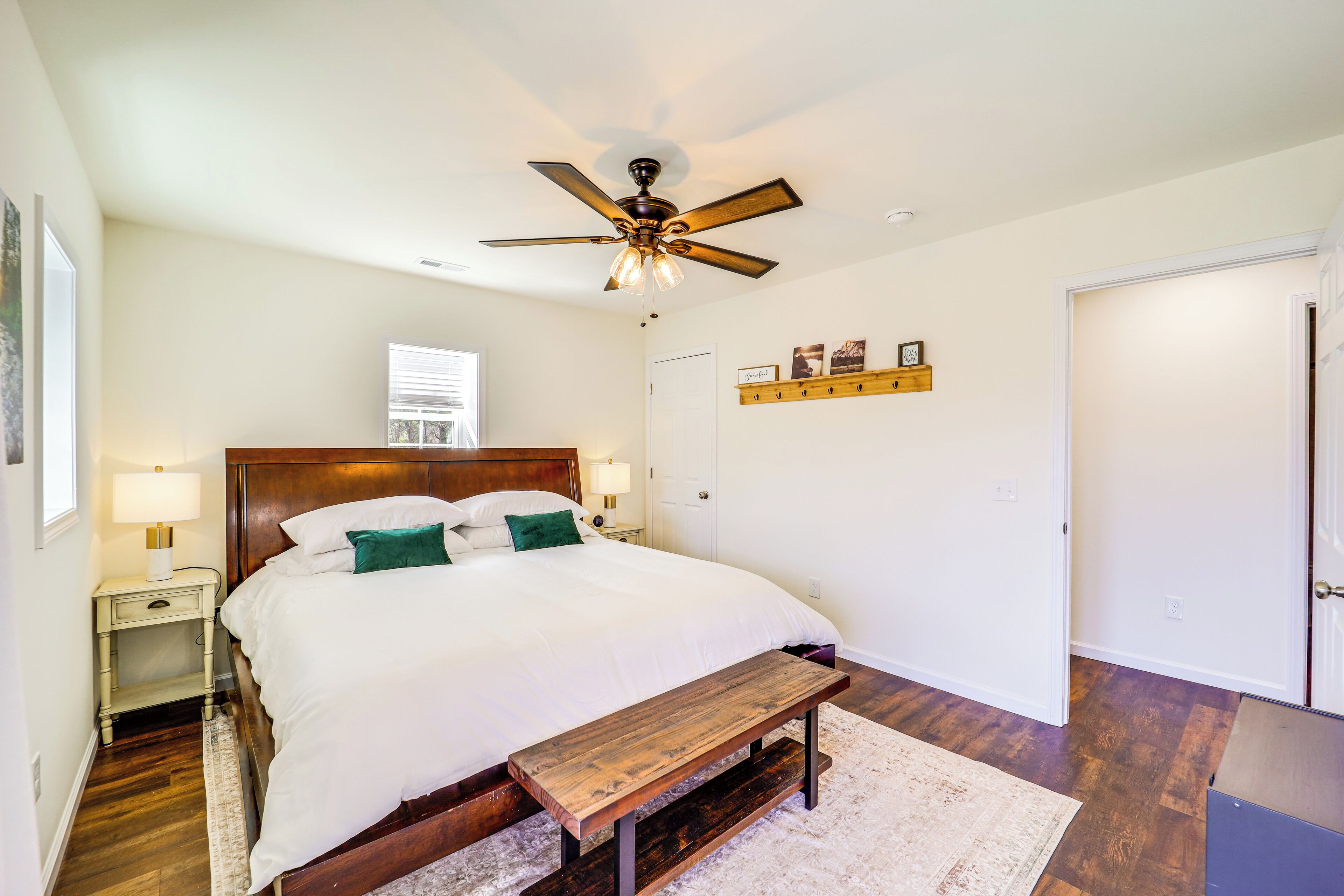 Une chambre à coucher avec un lit en bois, un ventilateur de plafond, une table de chevet, un banc et une porte.