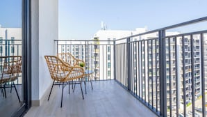 Un balcon avec des fauteuils en osier et une table, d’où l’on peut admirer une vue sur la ville, avec ses nombreux immeubles de grande hauteur.