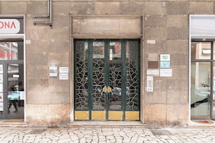 Fachada de edificio con una verja metálica verde, con los números 128 y 126, y un pavimento adoquinado en primer plano.