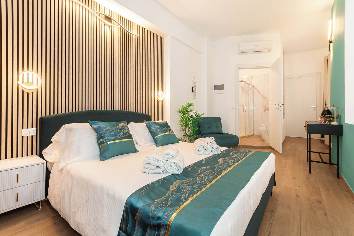 A neatly made bed with a green and white bedspread, a bedside table, and a wall-mounted light fixture.