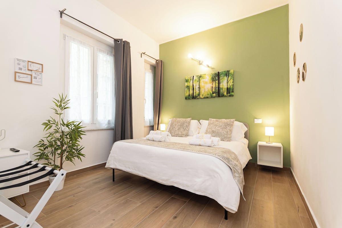 A neatly arranged hotel room with a bed, bedside lamps, a small table, and a potted plant.