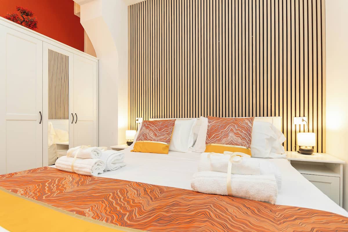 A hotel room with a large bed, a wardrobe, and a nightstand with a lamp.