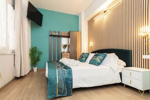 A modern bedroom with a bed, bedside tables, a TV, and a potted plant. - VittorioVeneto126 (La Spezia)