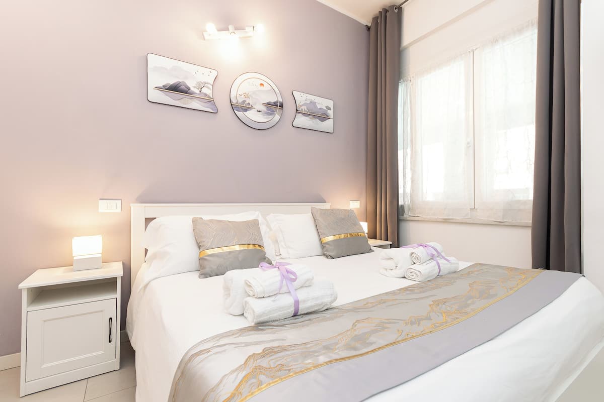 A neatly made bed with towels, a bedside table with a lamp, and wall art.