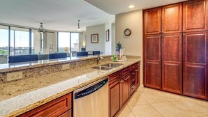 A modern kitchen with granite countertops, a dishwasher, wooden cabinets, and a large window offering a city view.