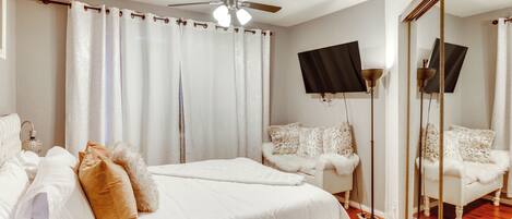 A bedroom with a bed, a chair, a ceiling fan, and a mirror.