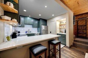 A modern kitchen with a central island, dark green cabinets, and a wooden ceiling. - Alpine Gondola Chalet (Steamboat Springs)