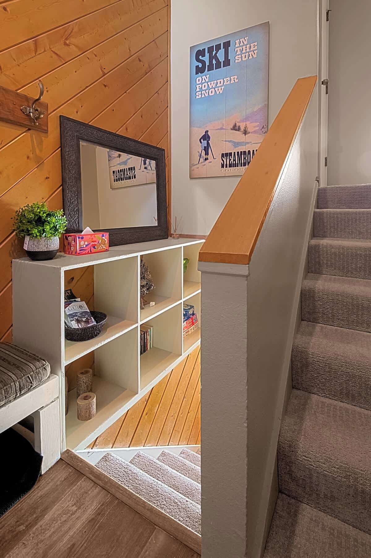 Een trap met houten leuning die uitkomt op een plateau waar een lijst met foto en een poster staan.