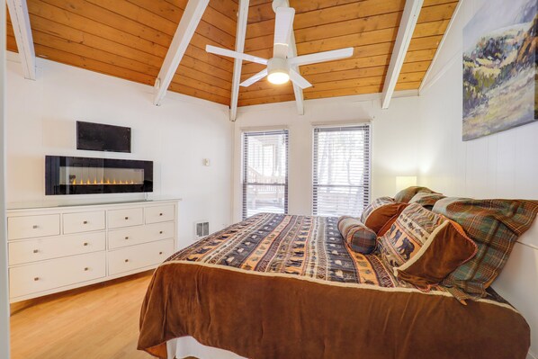 Une chambre avec un plafond en bois, un lit avec une literie à motifs, une commode blanche et un tableau accroché au mur.