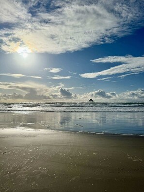 Une plage sous un ciel dégagé, avec le soleil qui se reflète sur le sable mouillé et les vagues qui se rapprochent du rivage.