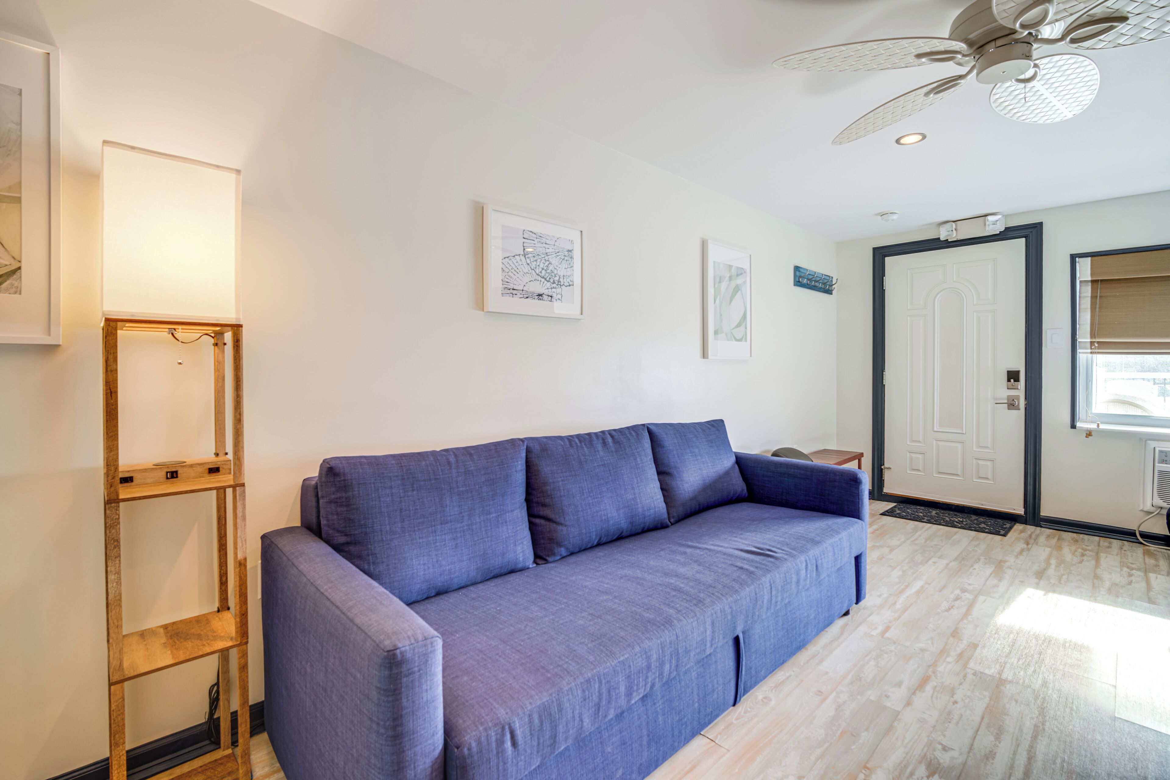 Una sala moderna con un sofá azul, una estantería escalonada de madera y un ventilador de techo.