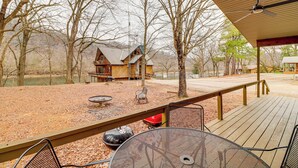 A wooden deck with a grill, chairs, and a view of a cabin by a lake. - Premier Trout Fishing: Scenic White River Cabin (Lakeview)