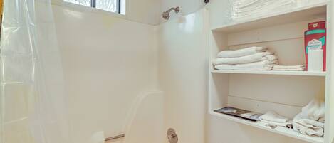 A bathroom with a shower, toilet, and shelves with towels and toiletries.