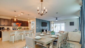 A modern kitchen with a central island, dining area with a wooden table and chairs, and a living area with a sofa and curtains.