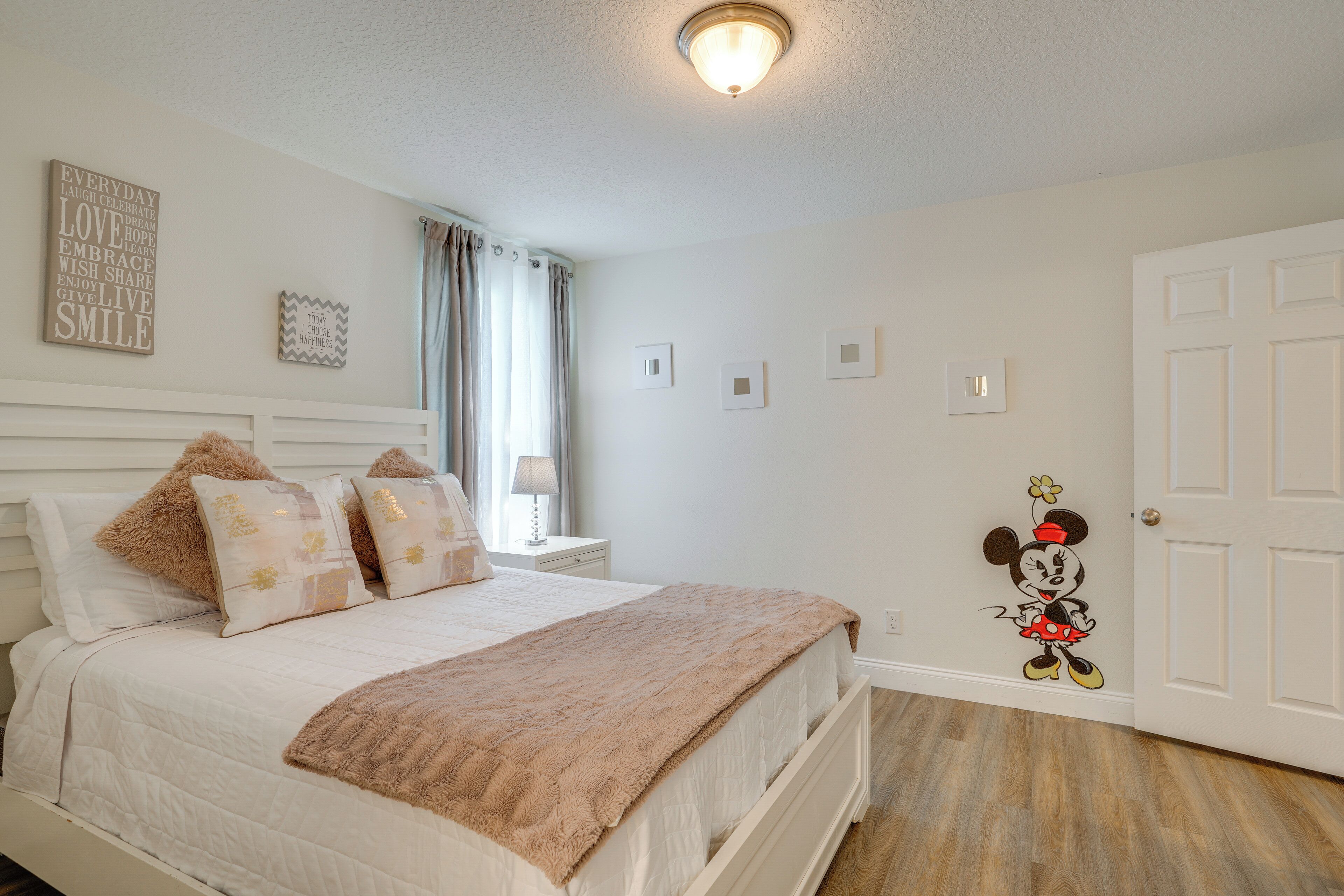 A bedroom with a bed, pillows, a nightstand, a lamp, a window with curtains, and a door.