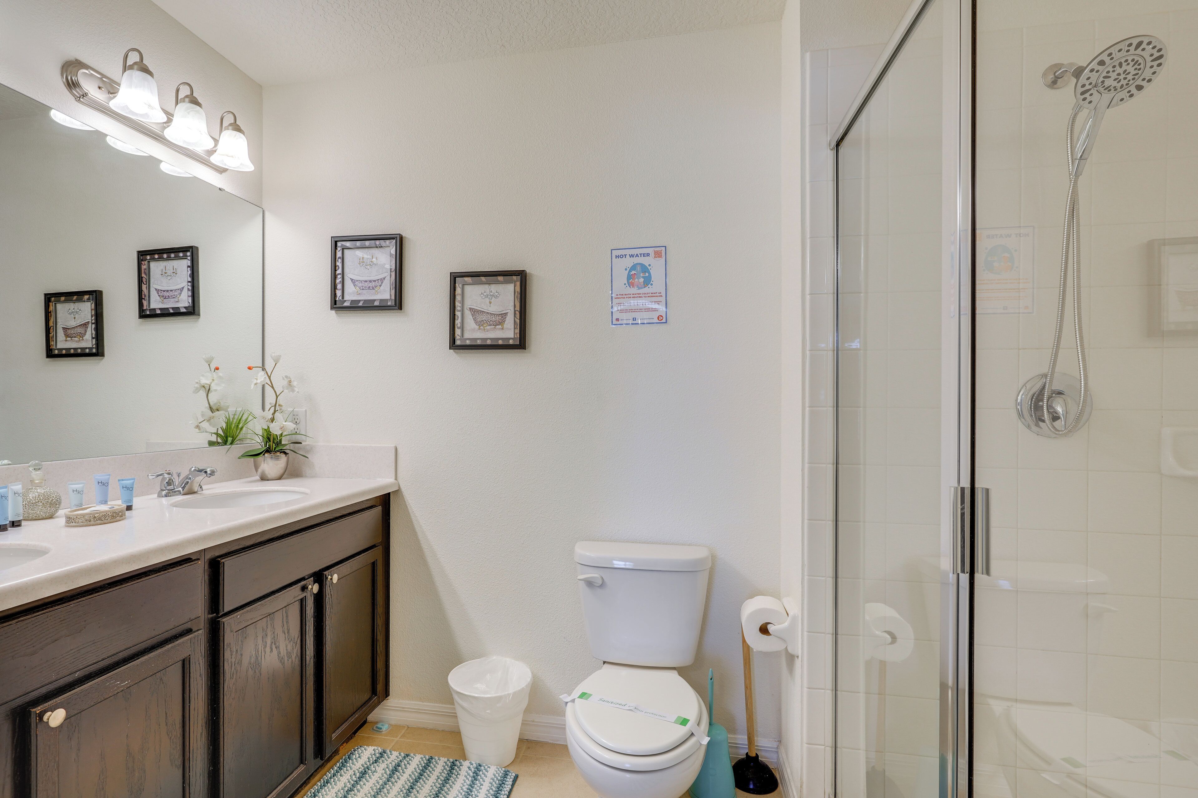 Une salle de bain avec un lavabo blanc, des meubles en bois foncé, des toilettes, une douche et des tableaux encadrés accrochés au mur.