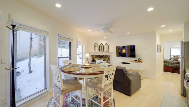 A modern living room with a round dining table, white chairs, a gray sofa, and a television mounted on the wall. - Ski, Hike & More! Couple's Getaway in Beech Mtn (Banner Elk)