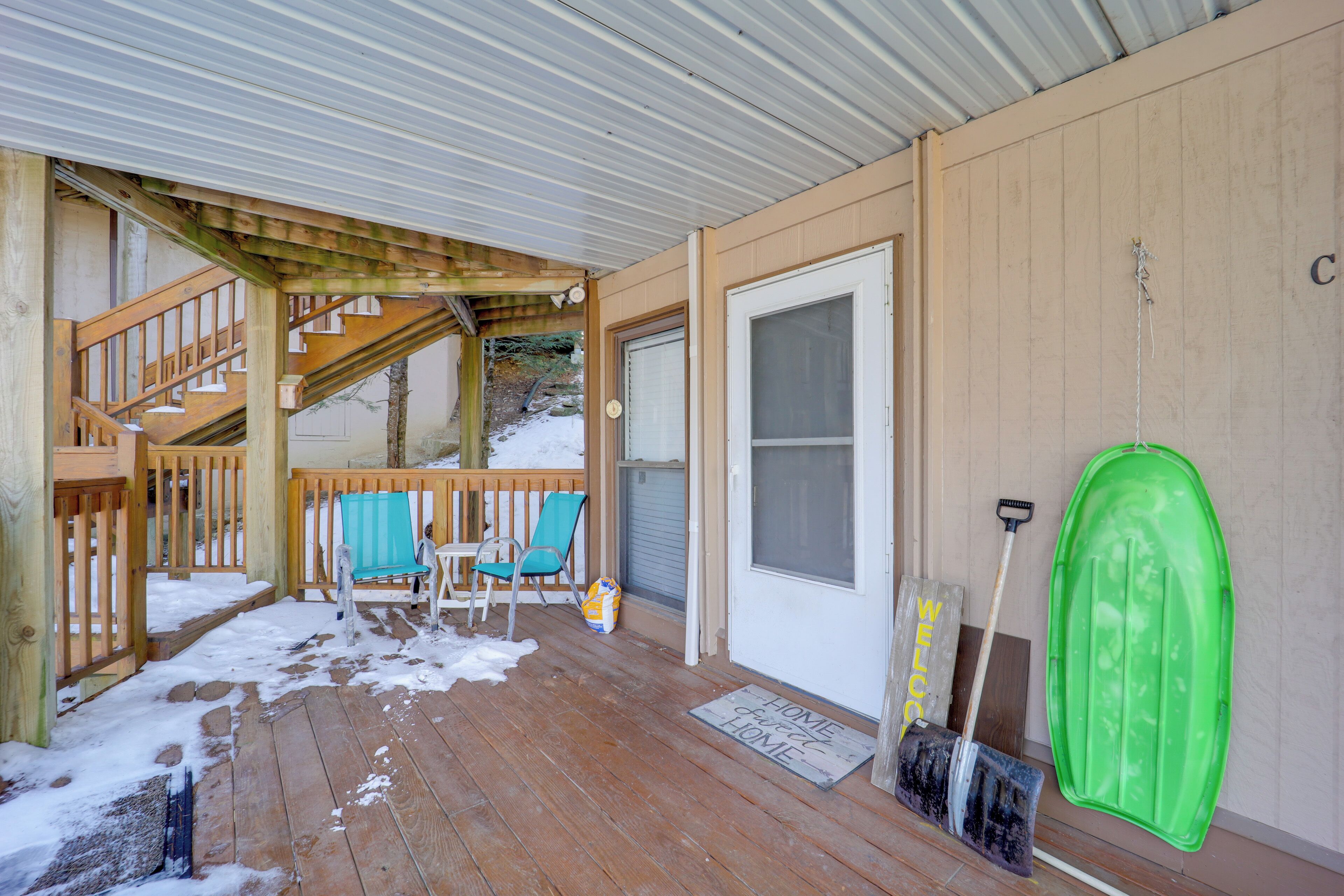 A wooden deck with a covered area, a door, and a green object hanging on the wall.