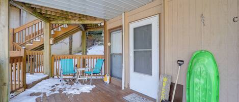 A wooden deck with a covered area, a door, and a green object hanging on the wall.
