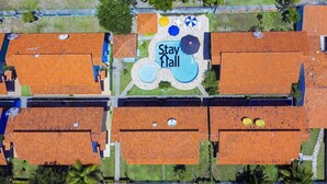 An aerial view of a residential area with multiple houses, a central courtyard with a 'Stay Hall' sign, and a swimming pool.