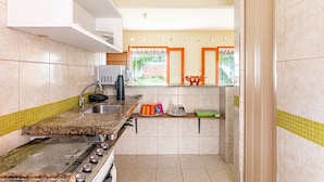 A compact kitchen with a gas stove, a microwave, and a sink. There are shelves with kitchen utensils and a window with a view of greenery.