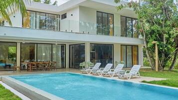 A modern two-story house with a swimming pool, outdoor seating, and large windows.