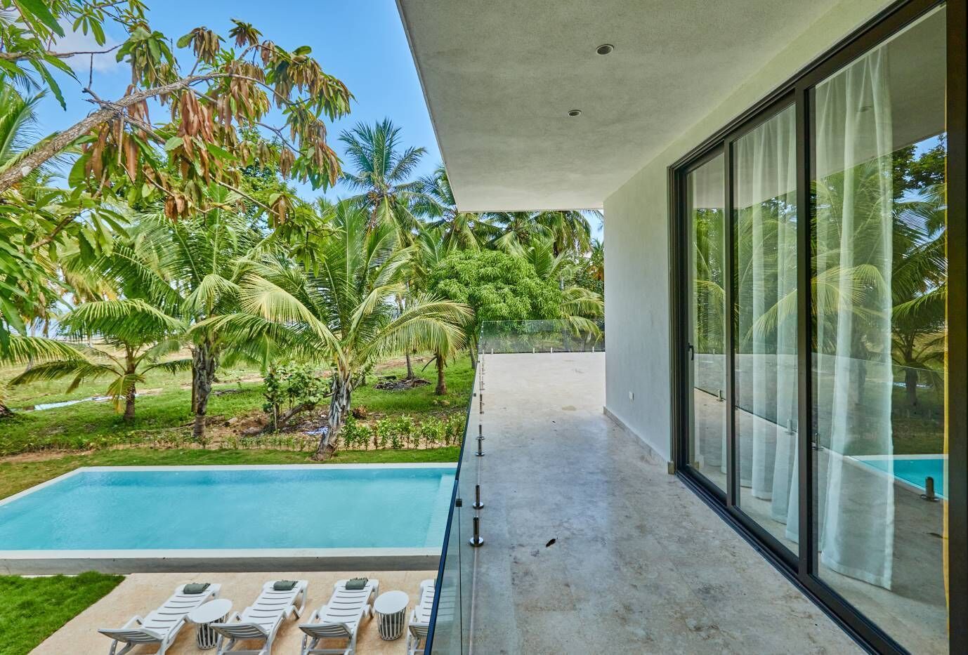 Um edifício moderno com varanda de vidro e vista para uma piscina e vegetação exuberante.