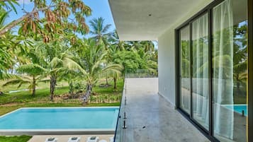 Um edifício moderno com varanda de vidro e vista para uma piscina e vegetação exuberante.