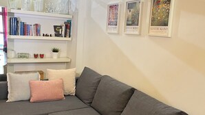 A modern living room with a grey sectional sofa, a white bookshelf, and three framed artworks on the wall.