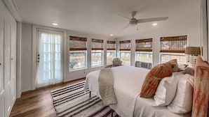 A bedroom with a bed, a ceiling fan, windows with blinds, a door, and a striped rug. - DT 332 Havana Haus (New Braunfels)