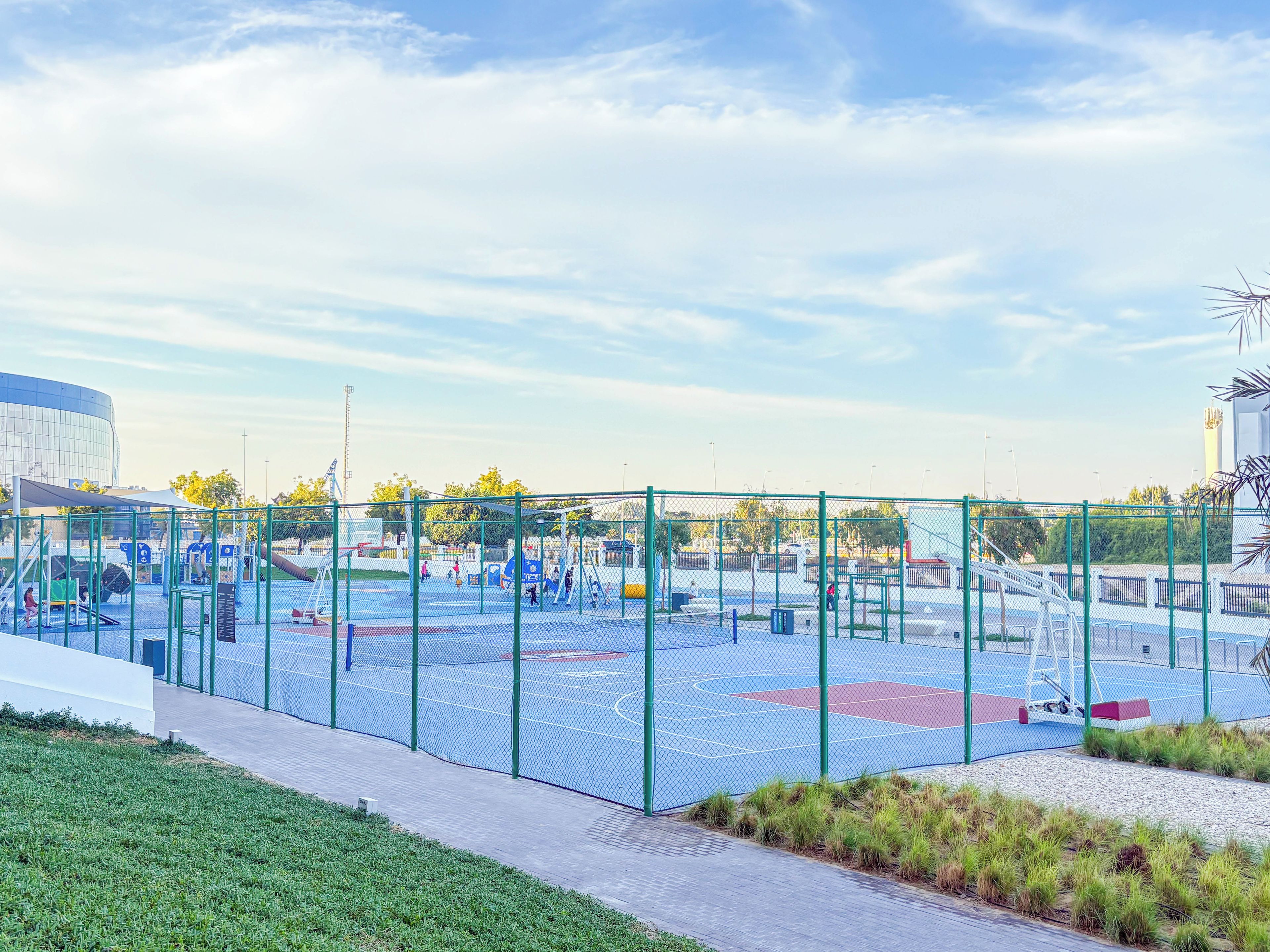 An outdoor sports facility with a basketball court, a playground, and a fenced area.